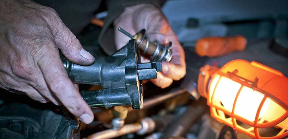 mechanic inspecting a car thermostat for signs of failure